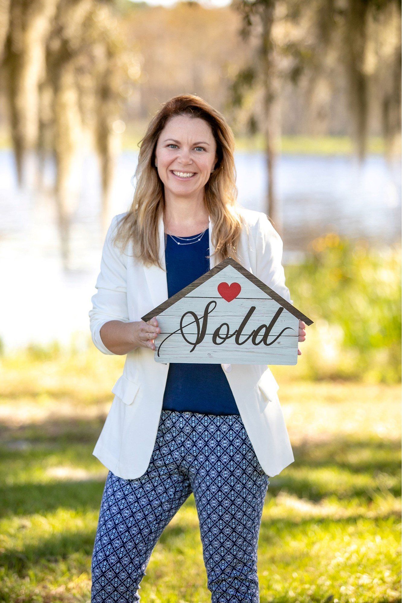 A woman is holding a sold sign in the shape of a house.