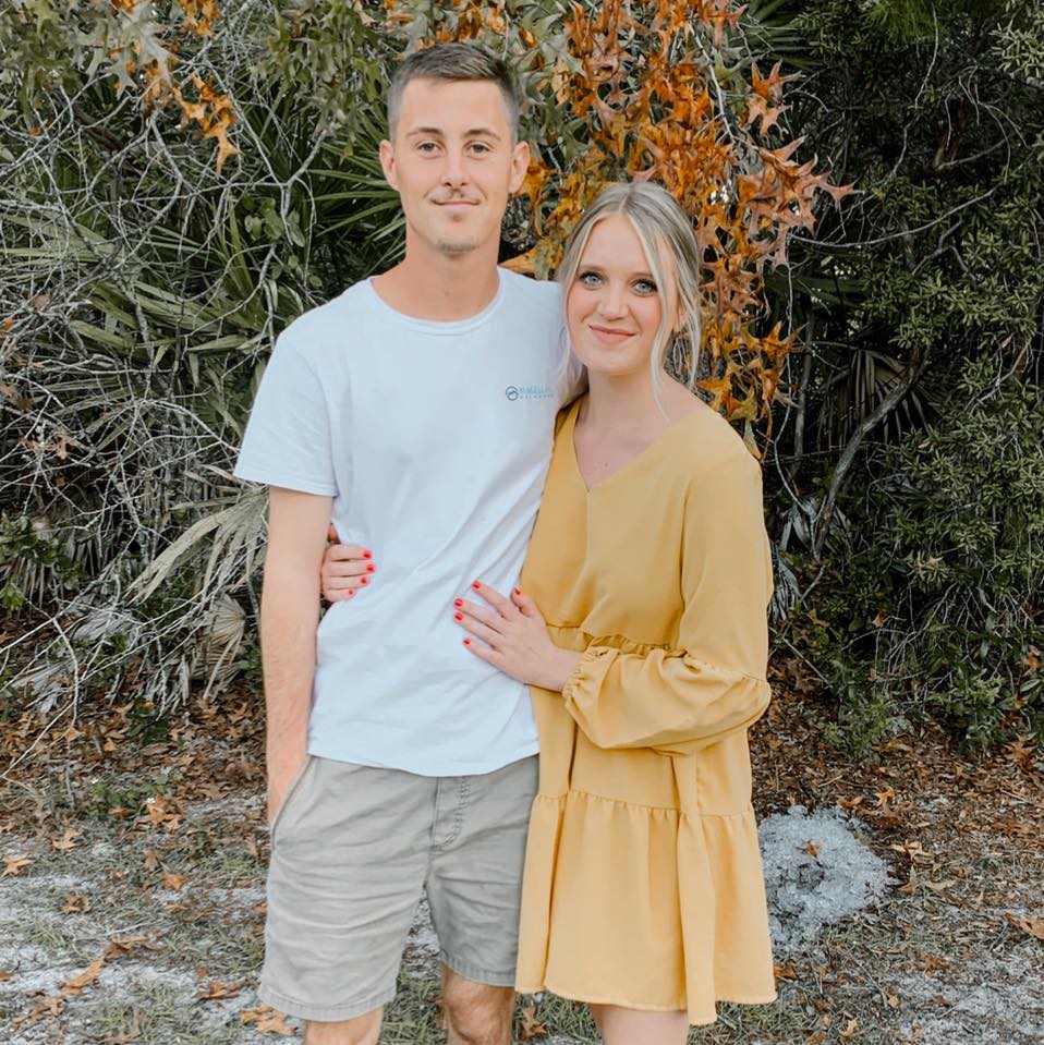 A man and a woman are posing for a picture together . the woman is wearing a yellow dress.