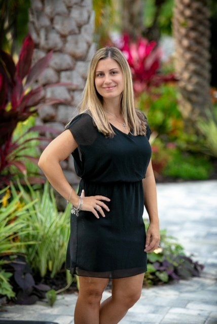 A woman in a black dress is standing in front of a garden.