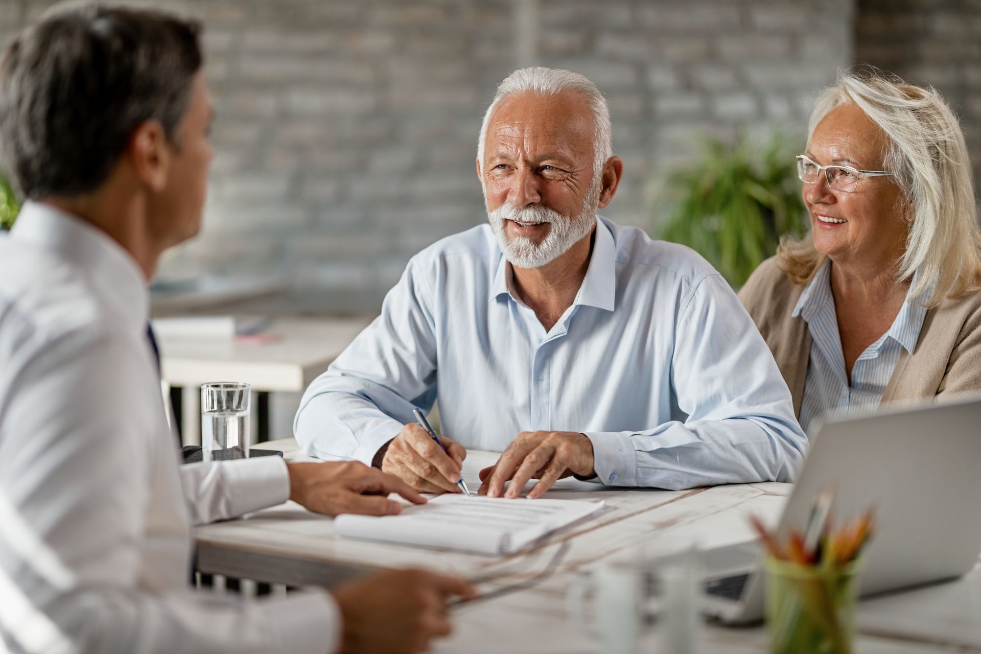 Woman in scrubs assisting a man seated in a chair, likely a caregiver and patient, in a home.