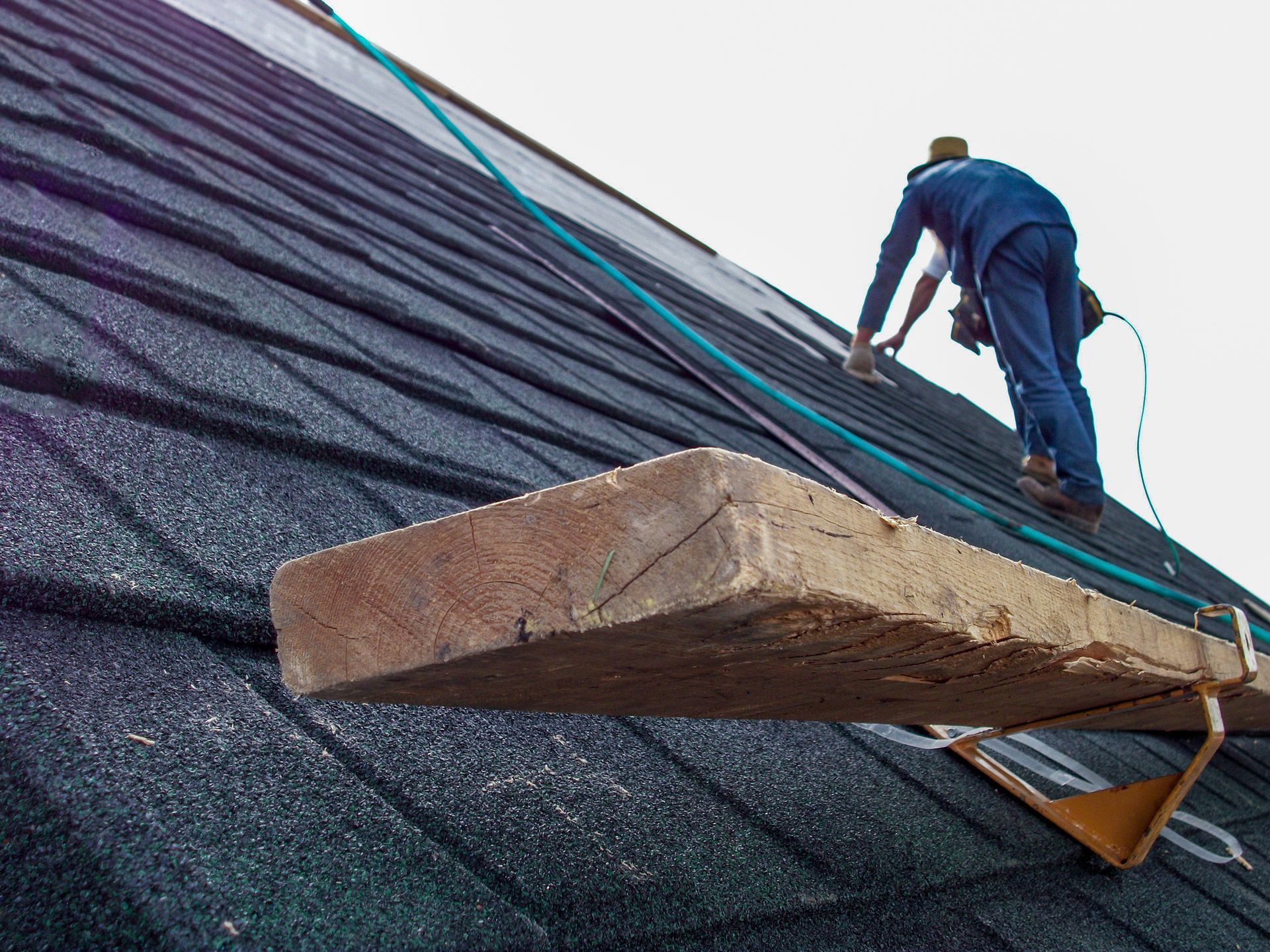 A worker is installing asphalt roof shingles  to a house.