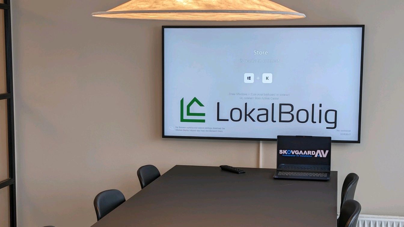 A conference room with a large flat screen tv and a laptop on the table.