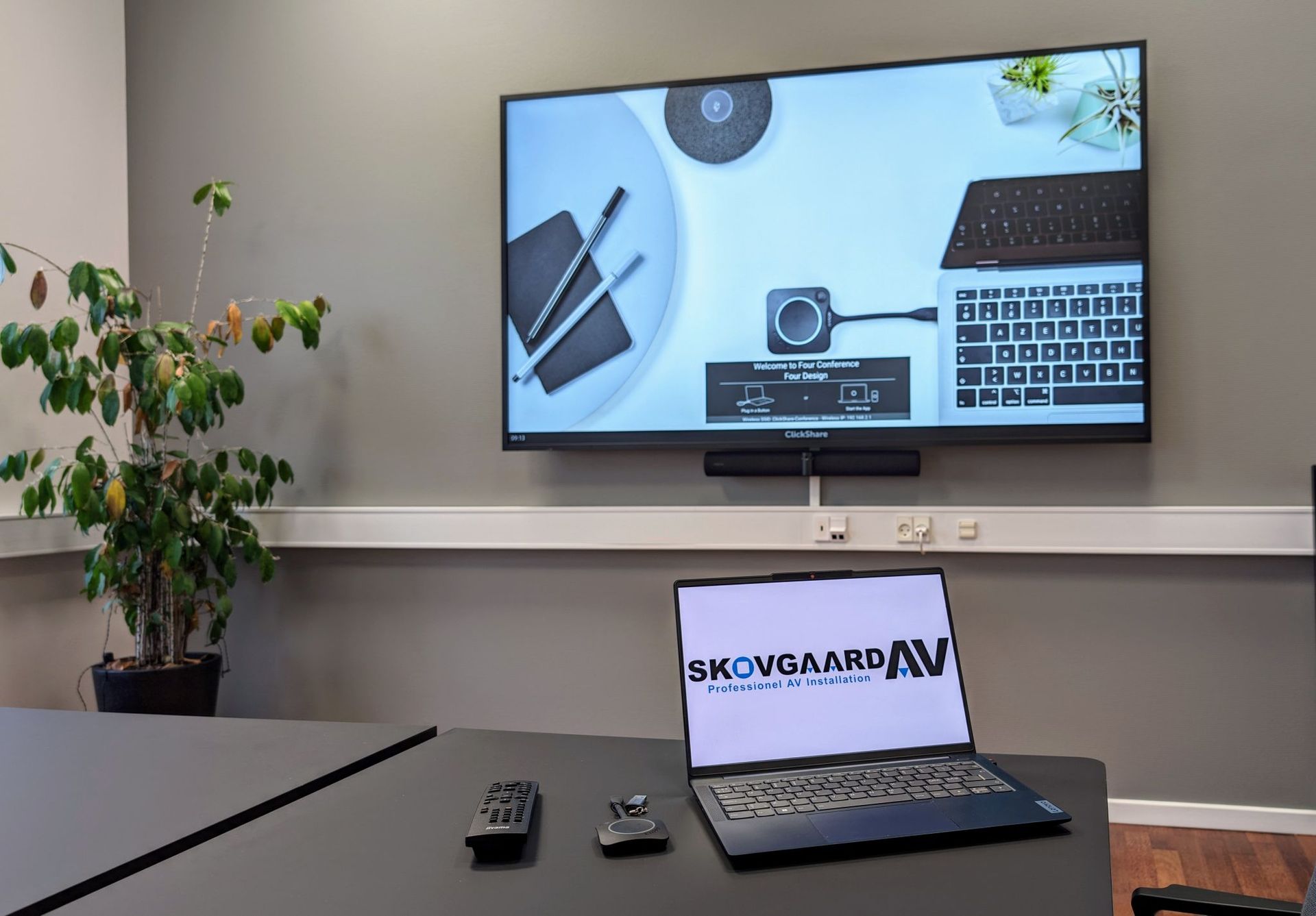 A laptop is sitting on a table in front of a large conference screen ready to hold a conference.