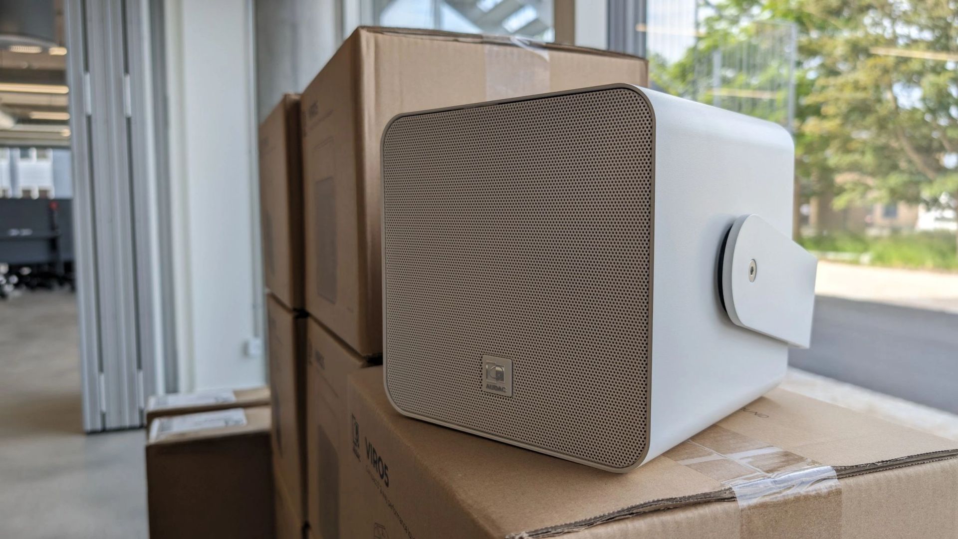 A white Audac Viso5 speaker is sitting on top of a stack of cardboard boxes.