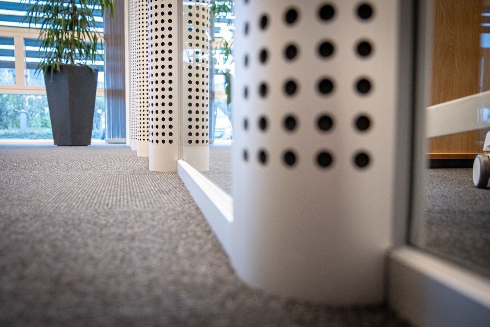 A close up of a carpeted floor in an office with a plant in the background and a glass wall.