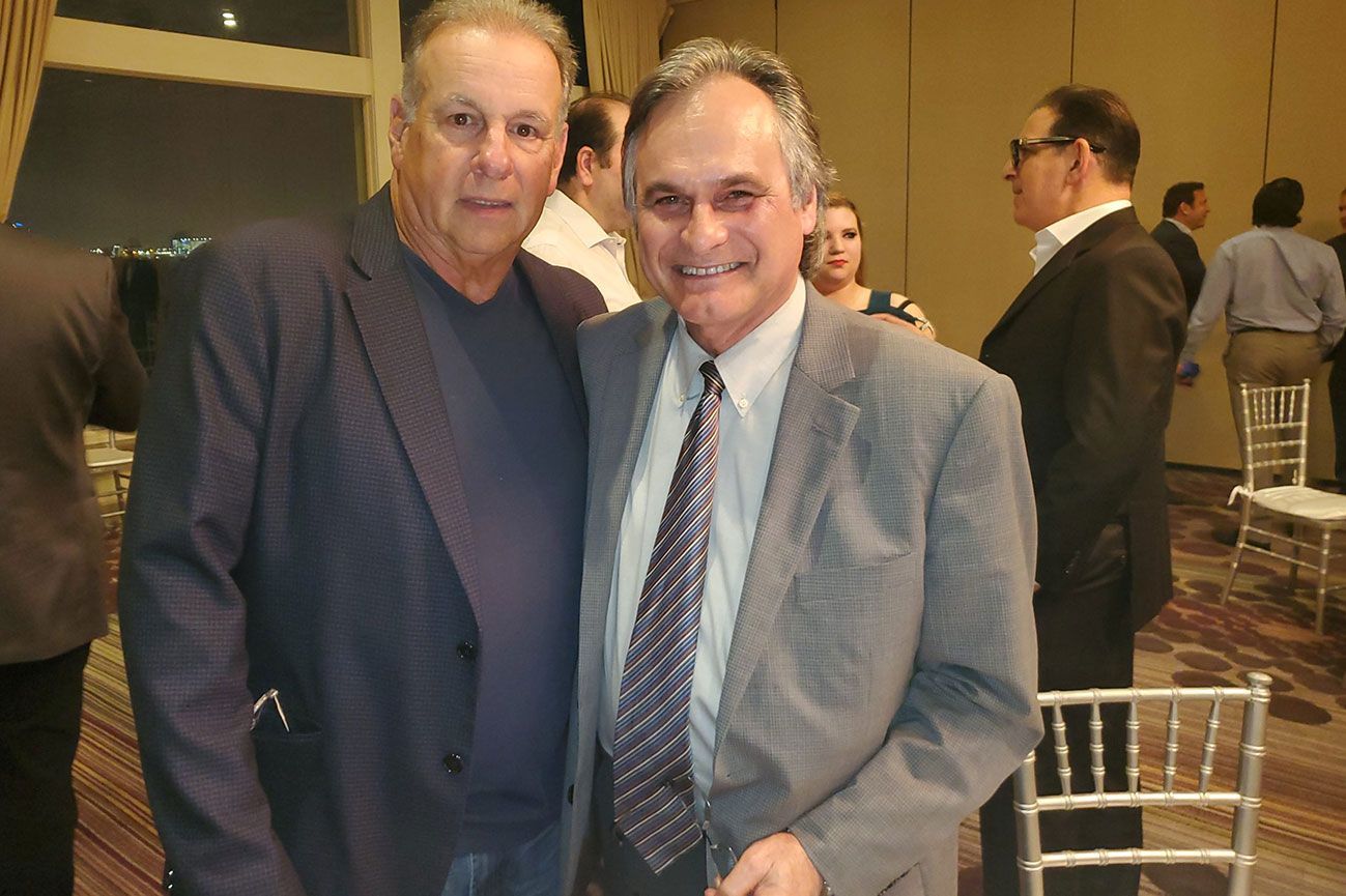 Two men in suits and ties pose for a picture