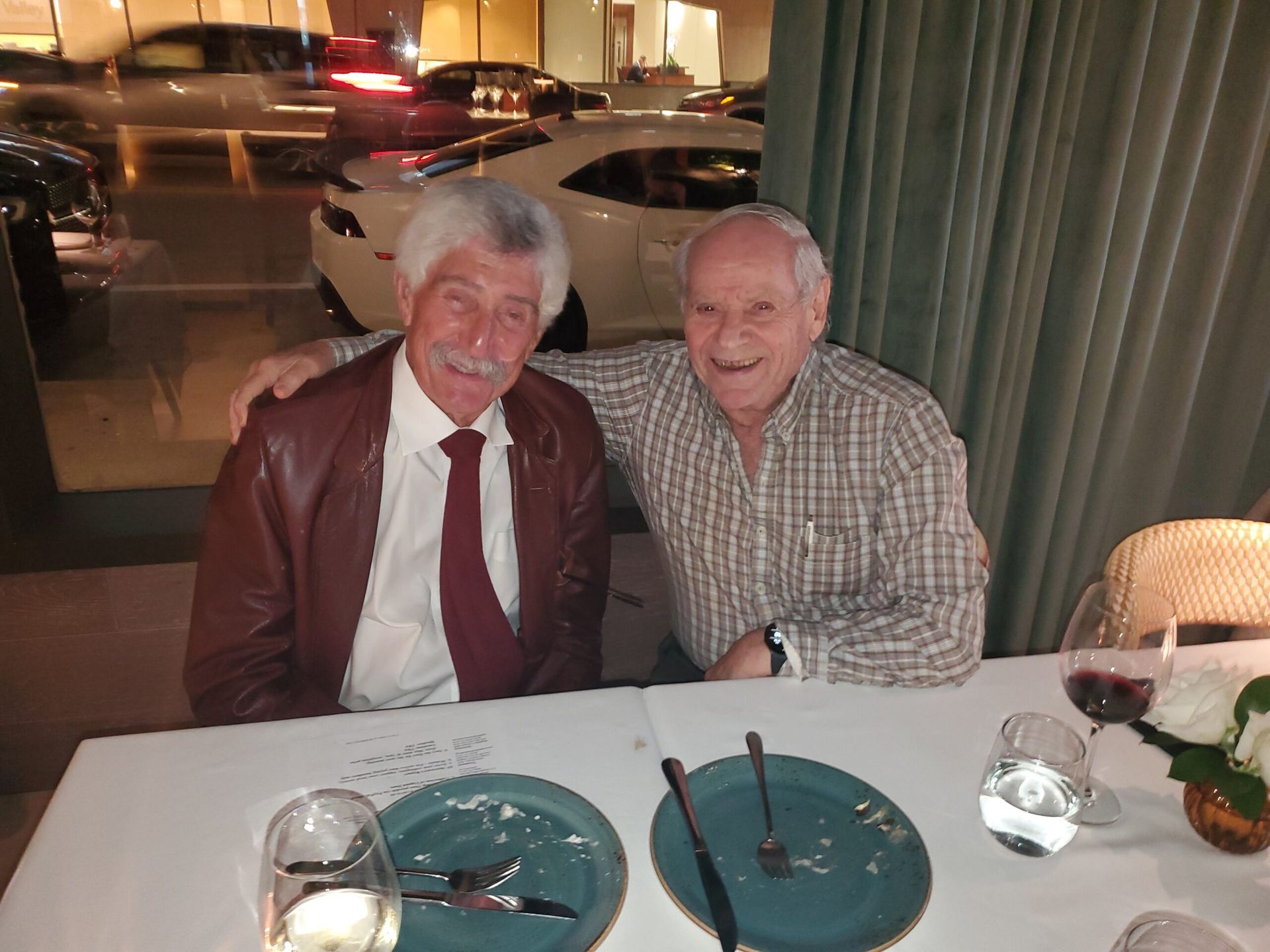 Two men are sitting at a table with plates and glasses of wine