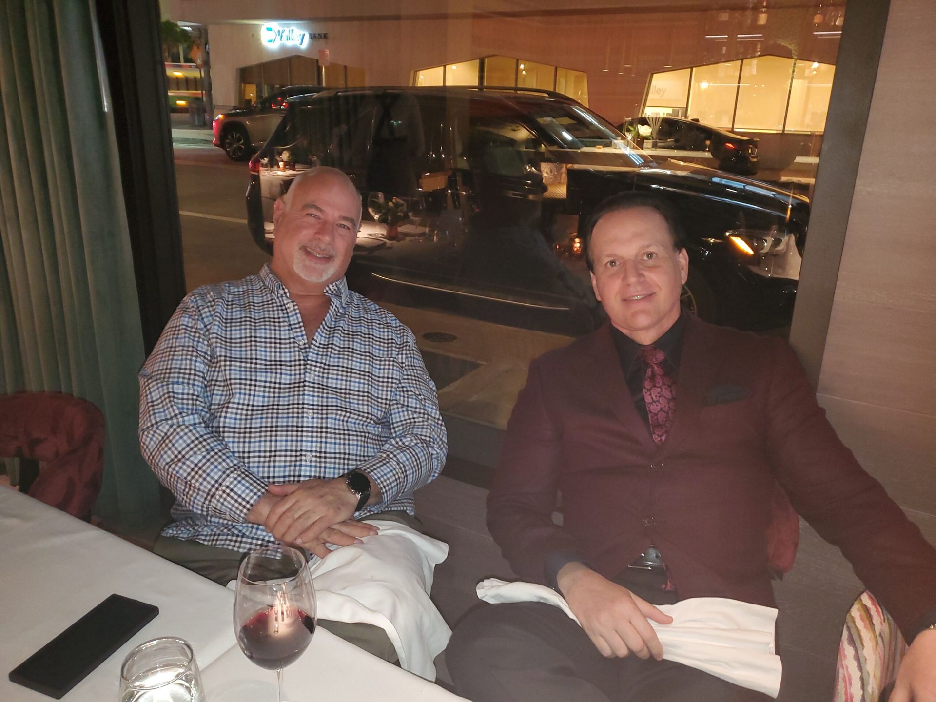 Two men are sitting at a table with a glass of wine.