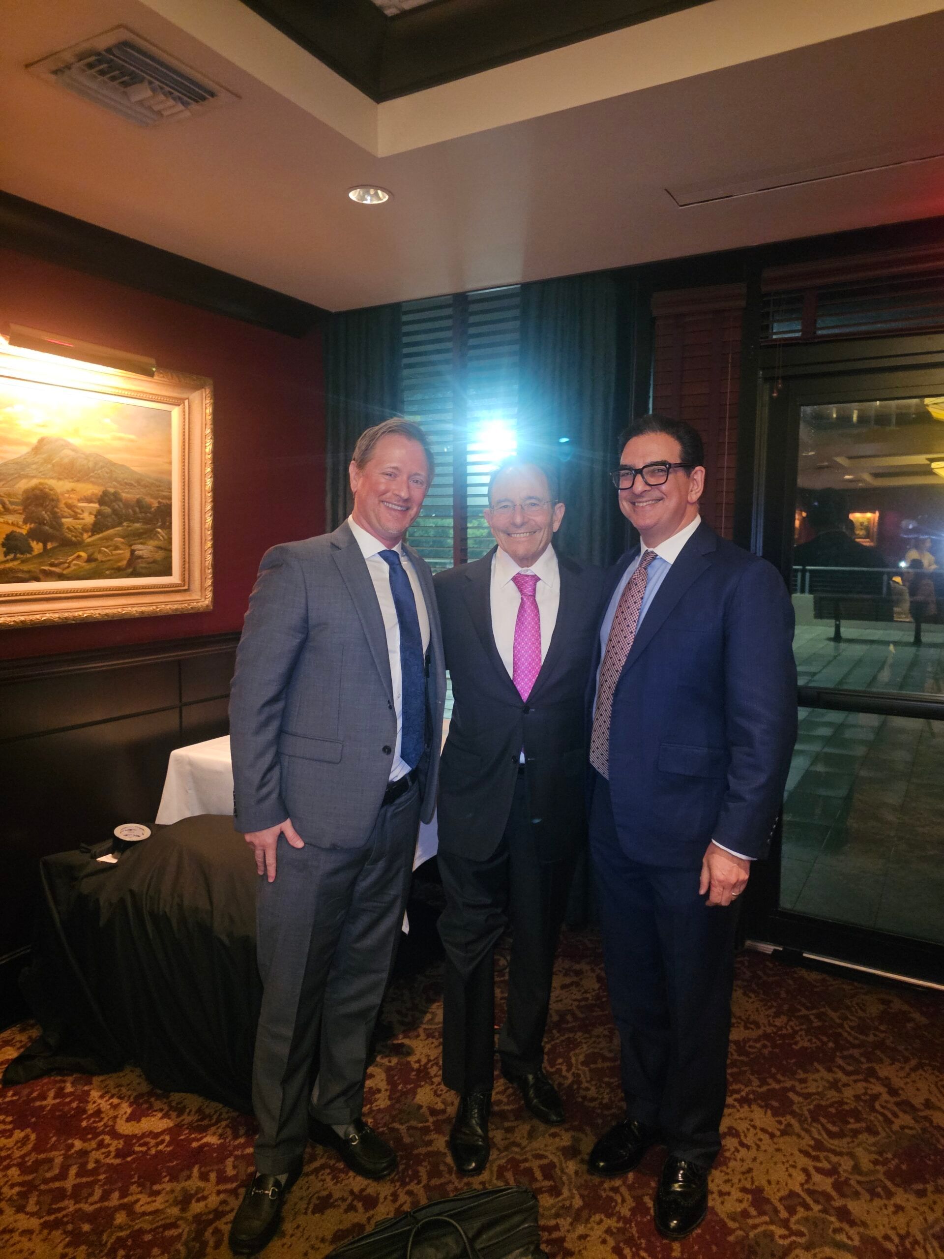 Three men in suits and ties are posing for a picture in a room.