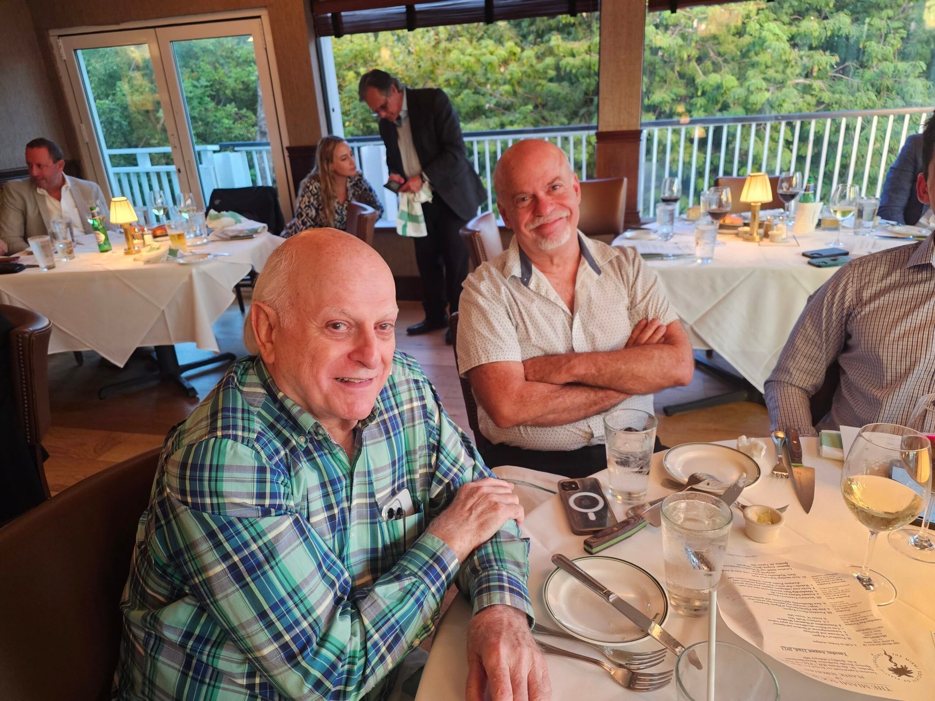 Two men are sitting at a table in a restaurant with their arms crossed.