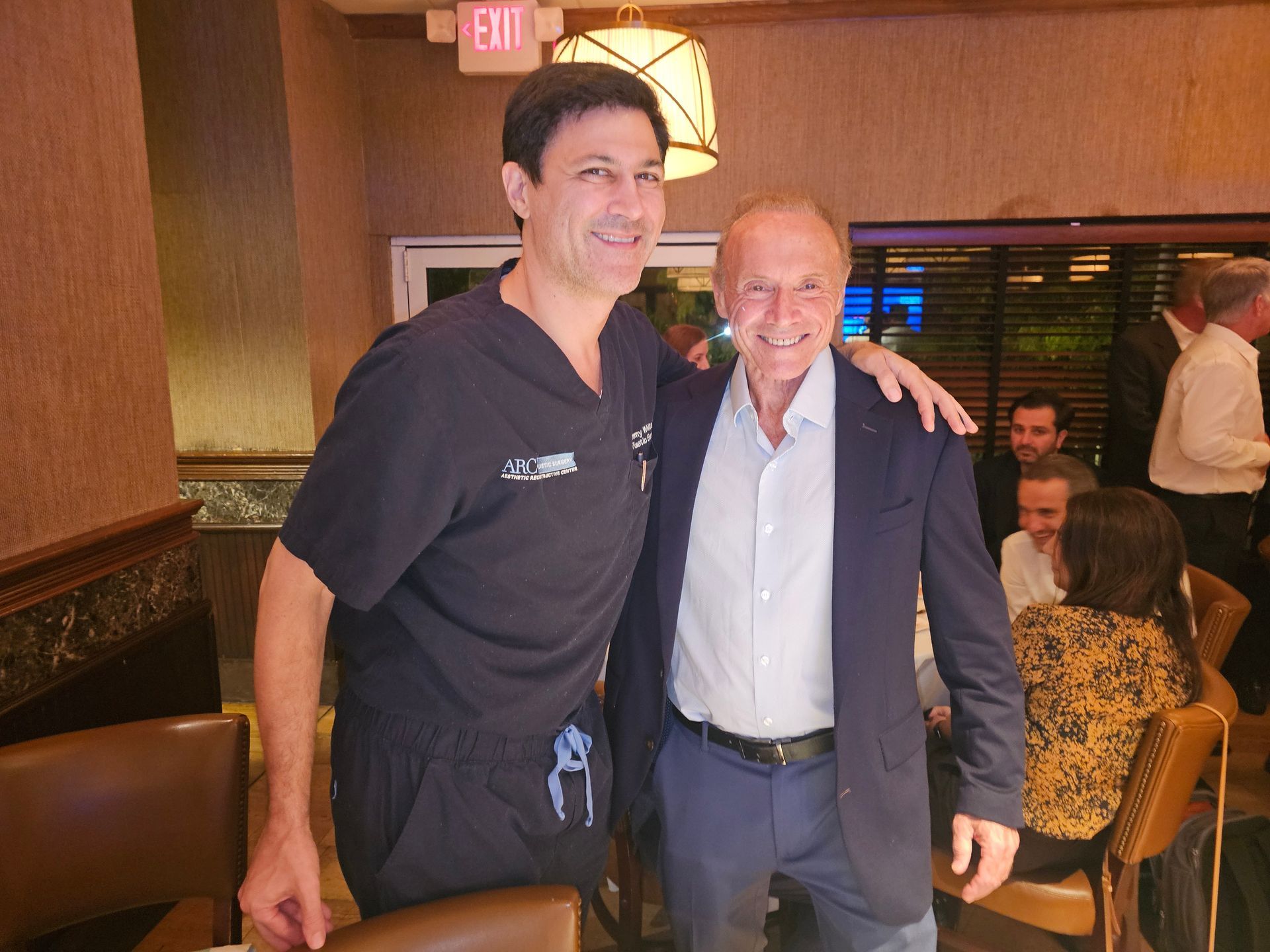 Two men posing for a picture in front of an exit sign