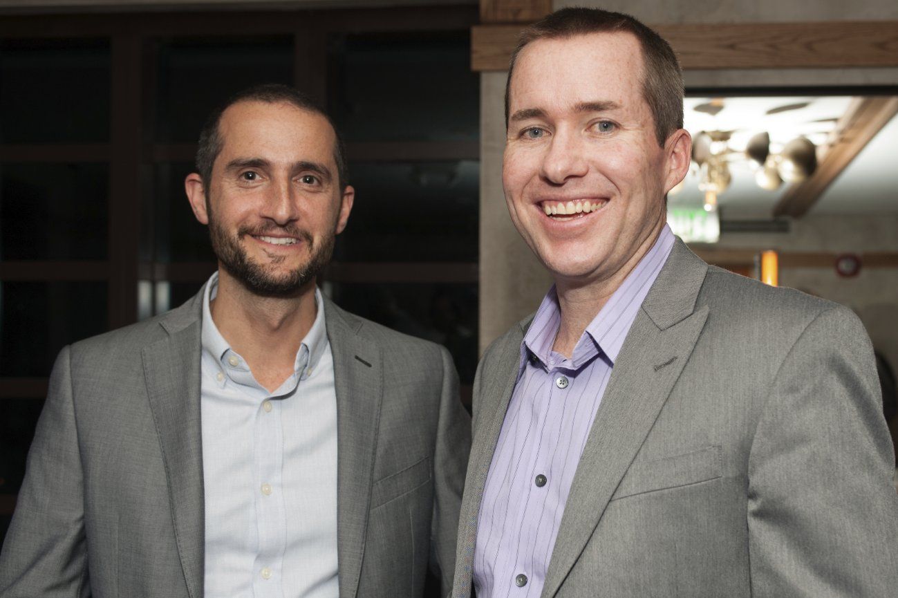 Two men in suits are standing next to each other and smiling.