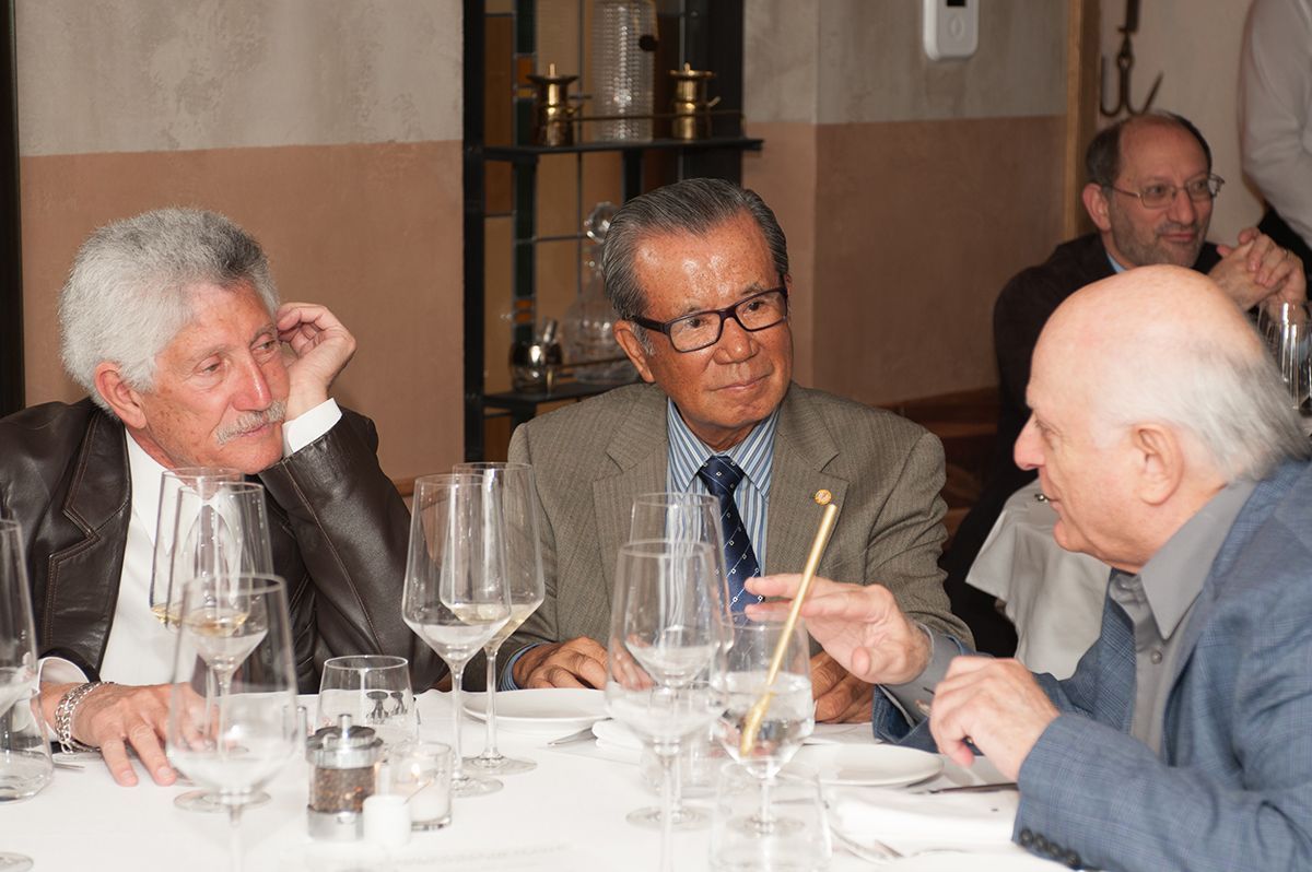 Three men are sitting at a table with wine glasses and talking.