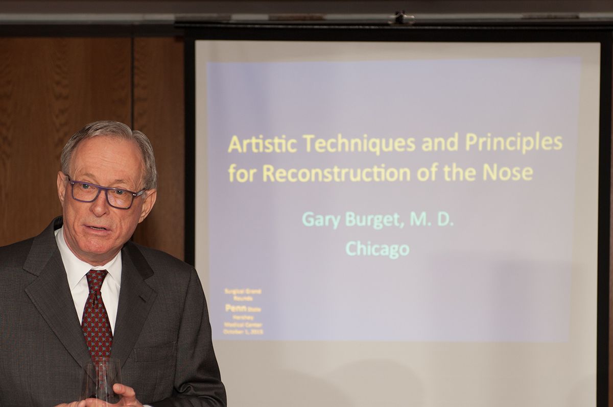 A man in a suit and tie is giving a presentation on artistic techniques and principles for reconstruction of the nose.