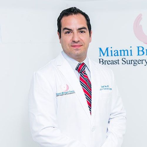 A man in a white coat and tie is standing in front of a sign for miami breast surgery.