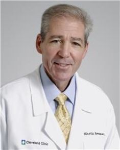 A man in a white coat and tie is smiling for the camera