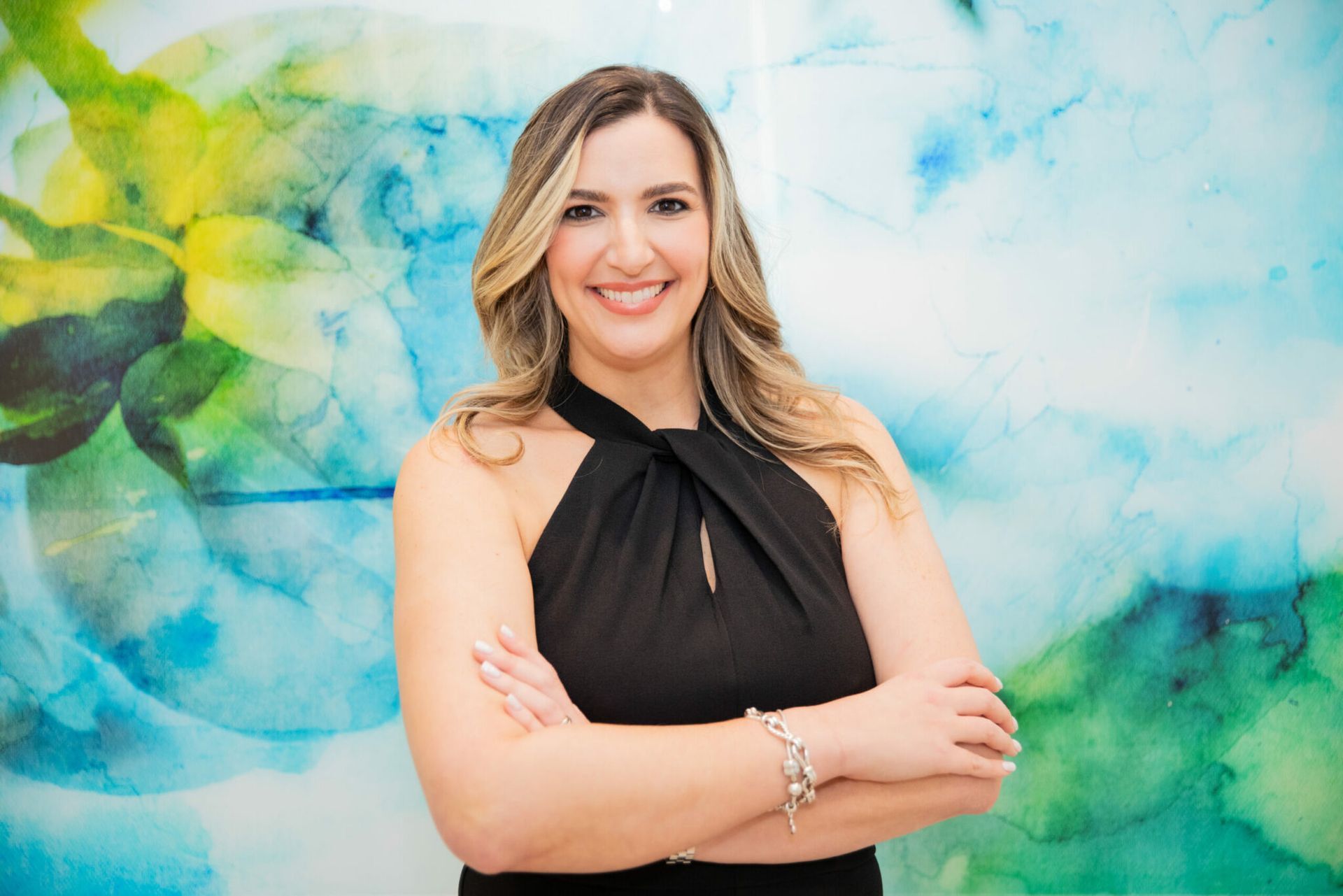 A woman in a black dress is standing with her arms crossed in front of a painting.