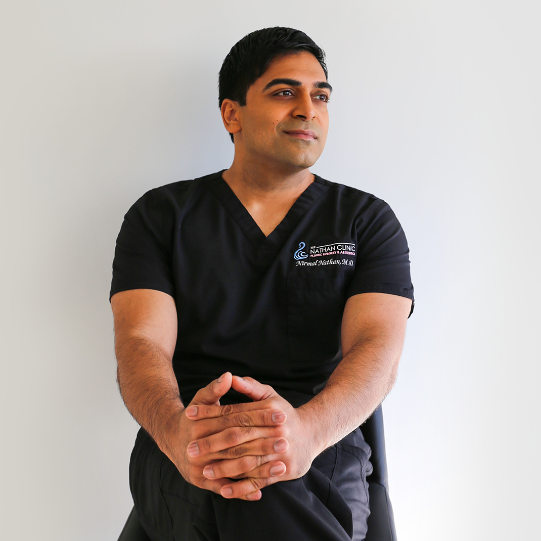 A man wearing a black scrub top is sitting with his hands folded