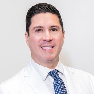 A man in a white coat and blue tie is smiling for the camera.