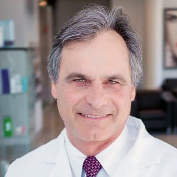 A man in a white coat and tie is smiling for the camera.