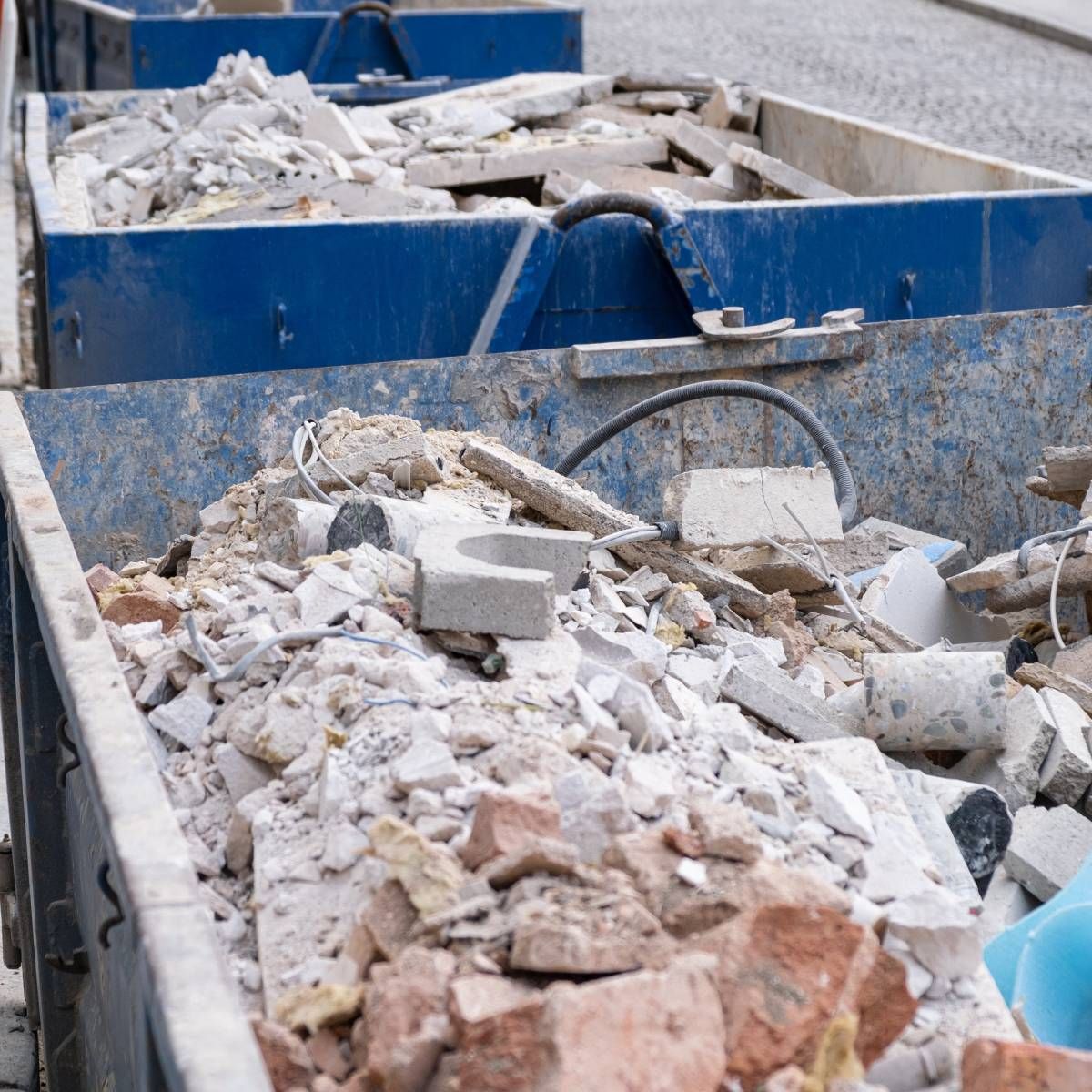 Two blue metal dumpsters filled with construction debris: broken bricks, concrete, and rubble.