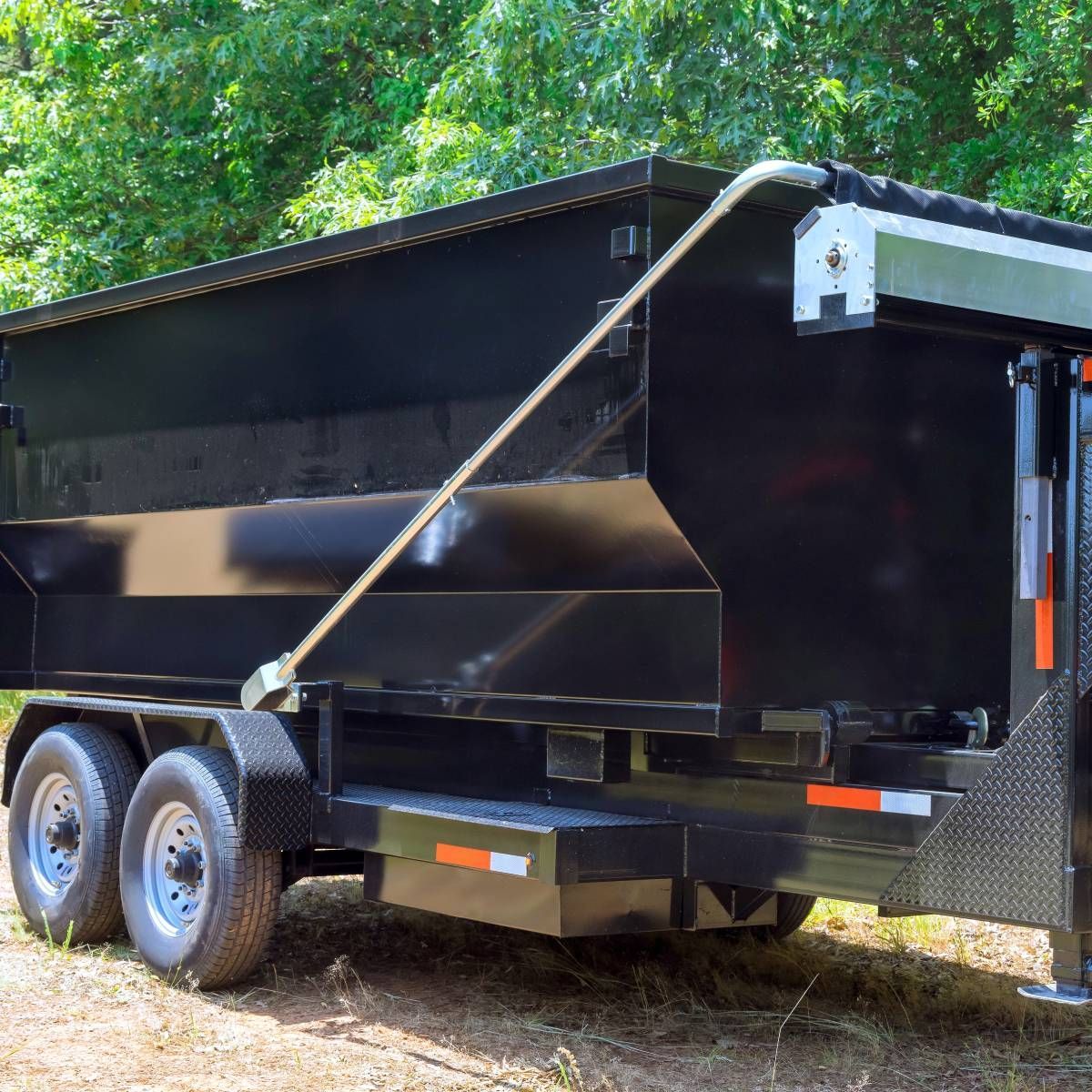 Black dump trailer parked outdoors with two wheels visible.