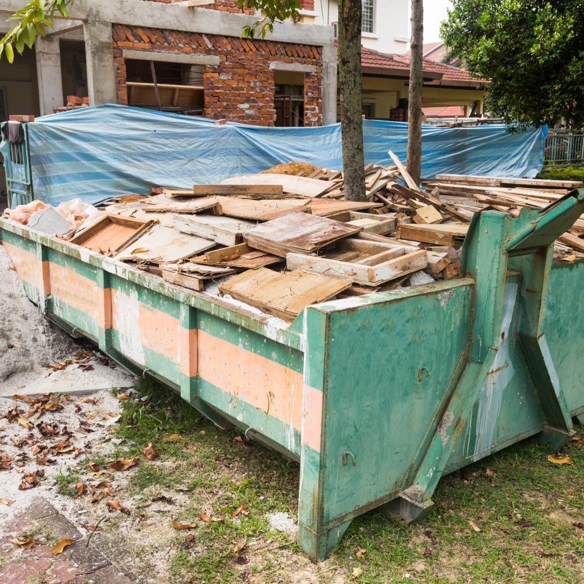 Green and orange dumpster filled with construction debris on a grassy area in front of a building under renovation.