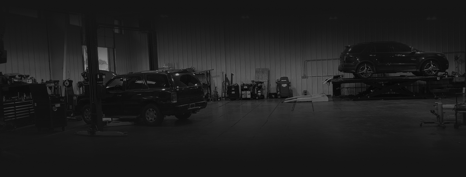 A dimly lit auto repair shop with two cars, one on a lift | The SouthSide Garage