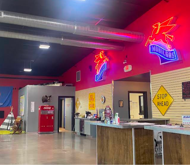 Interior of a business with red walls, neon signs, and a service counter. A Stop Ahead sign is visible | The SouthSide Garage