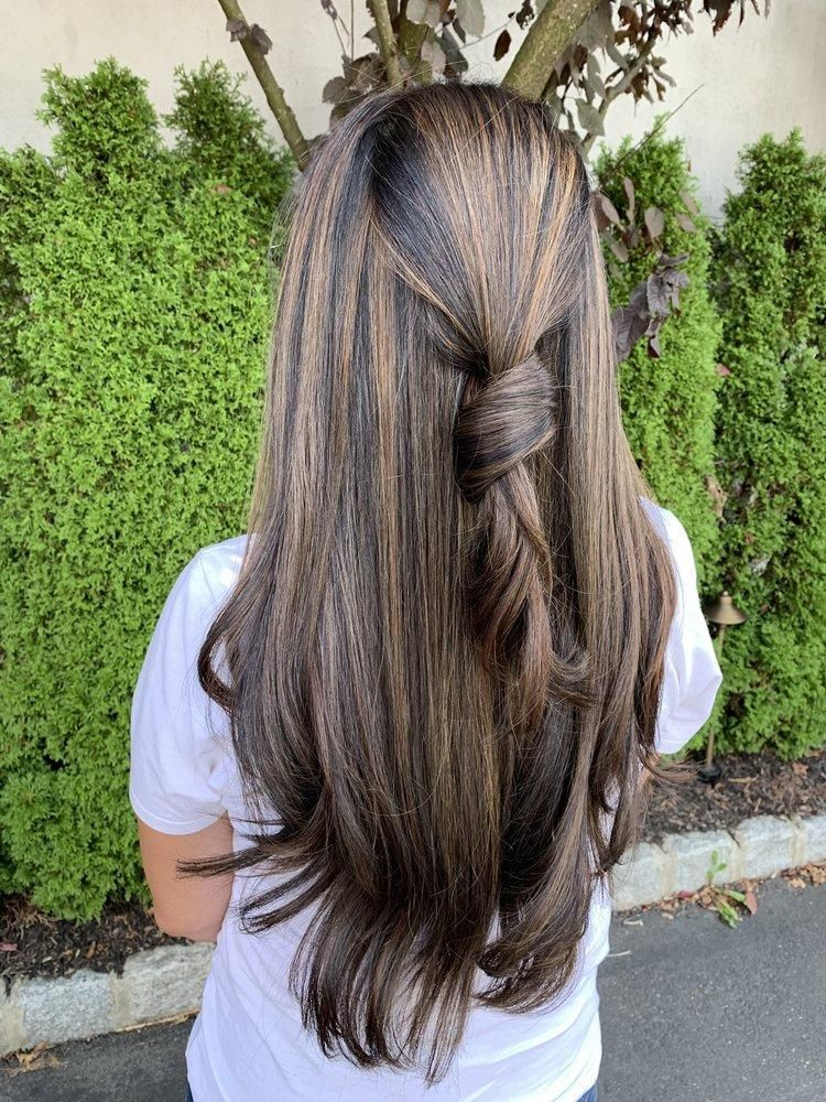 Woman with long, brown hair styled with a twisted section in the back.  Green foliage is behind her.
