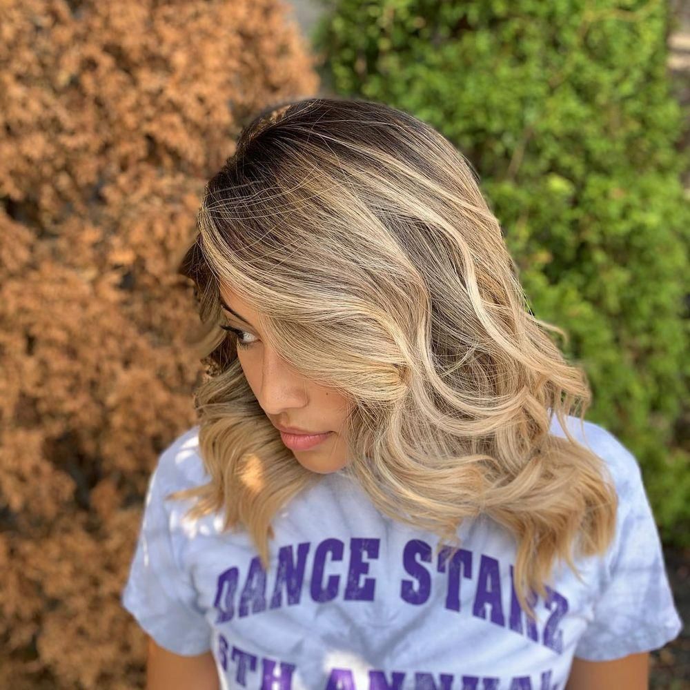 Woman with wavy blonde hair, wearing a tie-dye shirt, outdoors.