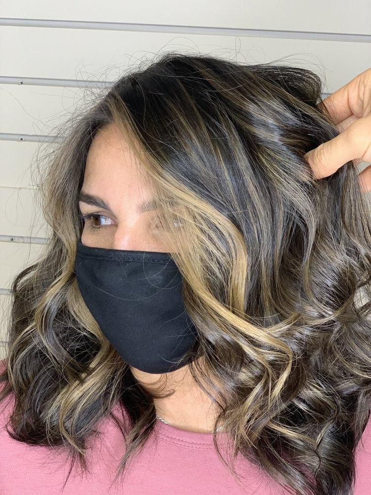 Woman with dark hair, blonde highlights, wearing a black face mask, styled in loose curls.