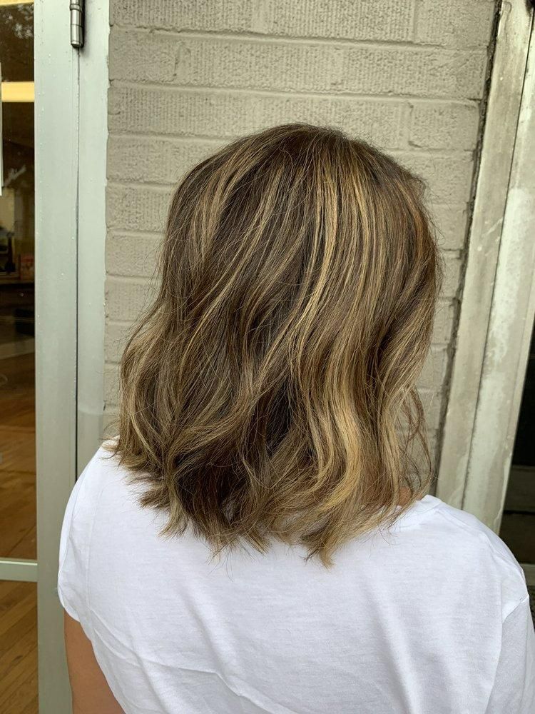 Woman's shoulder-length hair styled with highlights and waves against a brick wall.