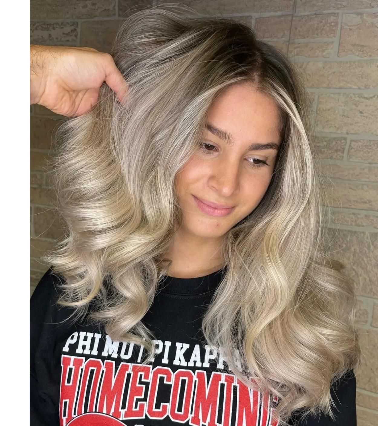 Woman with wavy blonde hair, light skin, smiling, wearing a black sweatshirt, indoors.