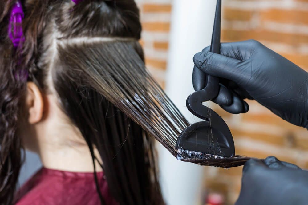 Hairdresser applying product to hair with a black applicator, in a salon.