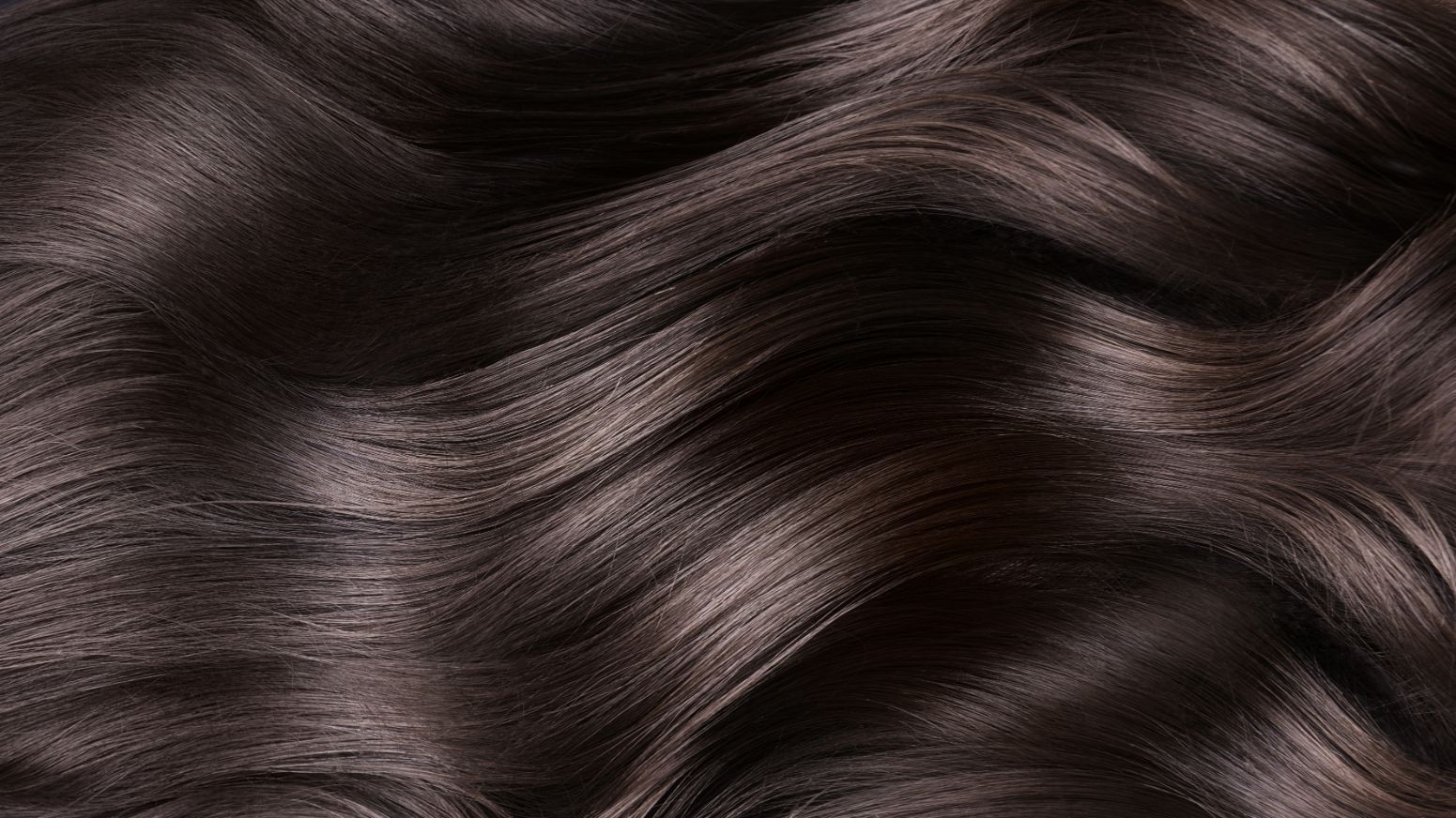 Close-up of smooth, dark brown wavy hair, with highlighted strands catching the light.