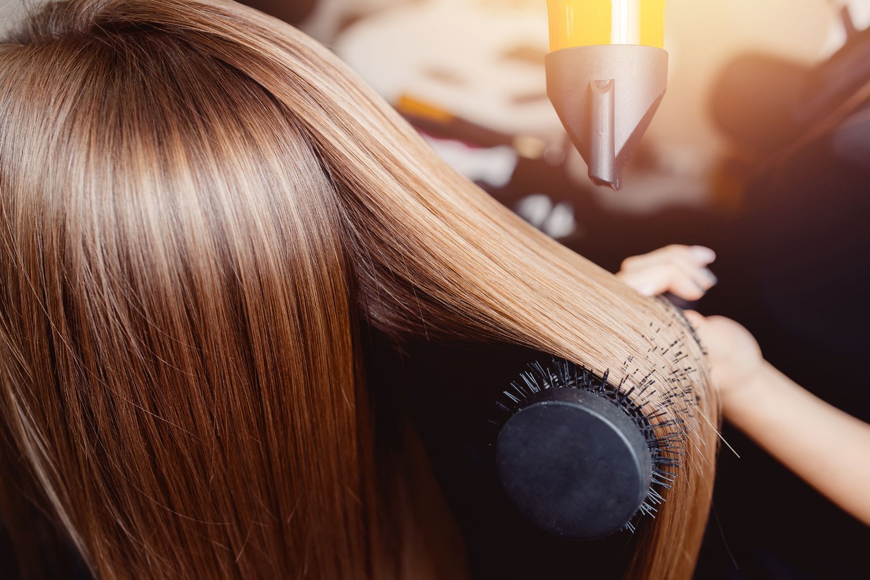 Hair being styled with a round brush and hairdryer, indoors.