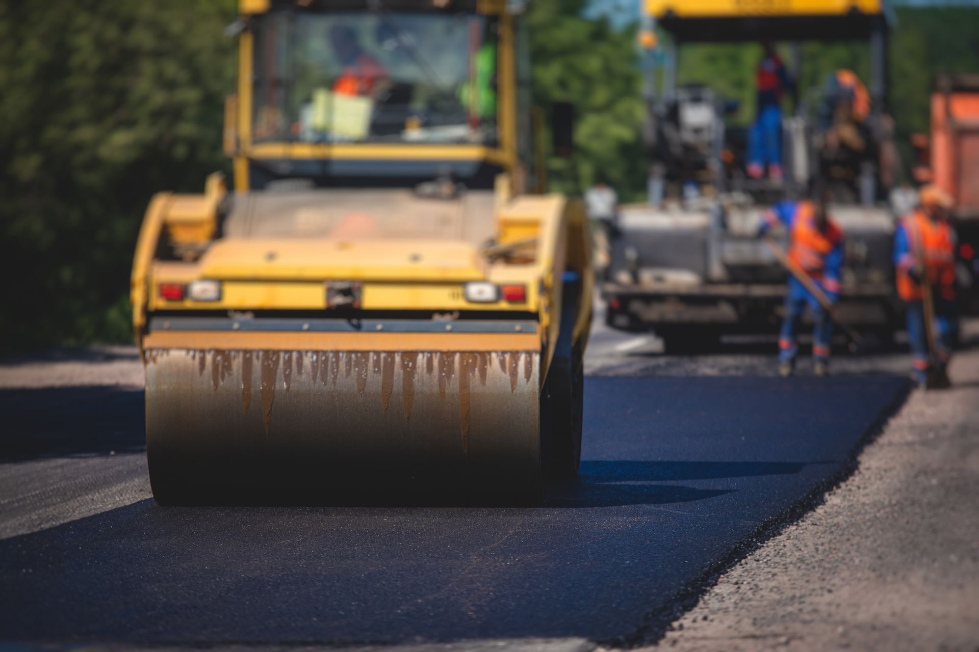 Picture of a steamroller and a group of industrial asphalt contractors working on road construction