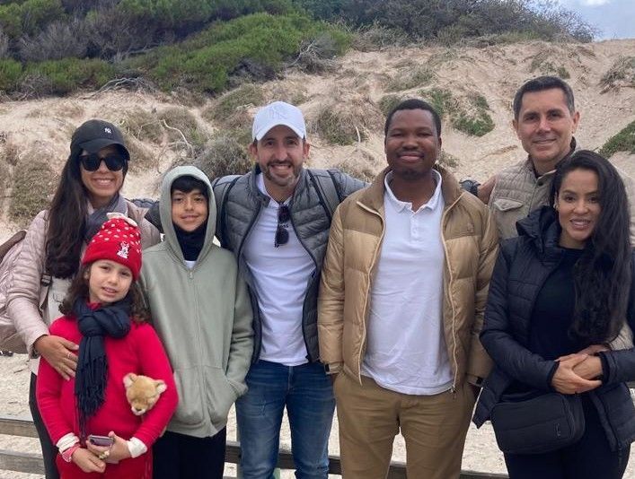Group of people smiling in an outdoor setting; some are wearing jackets, others hats.