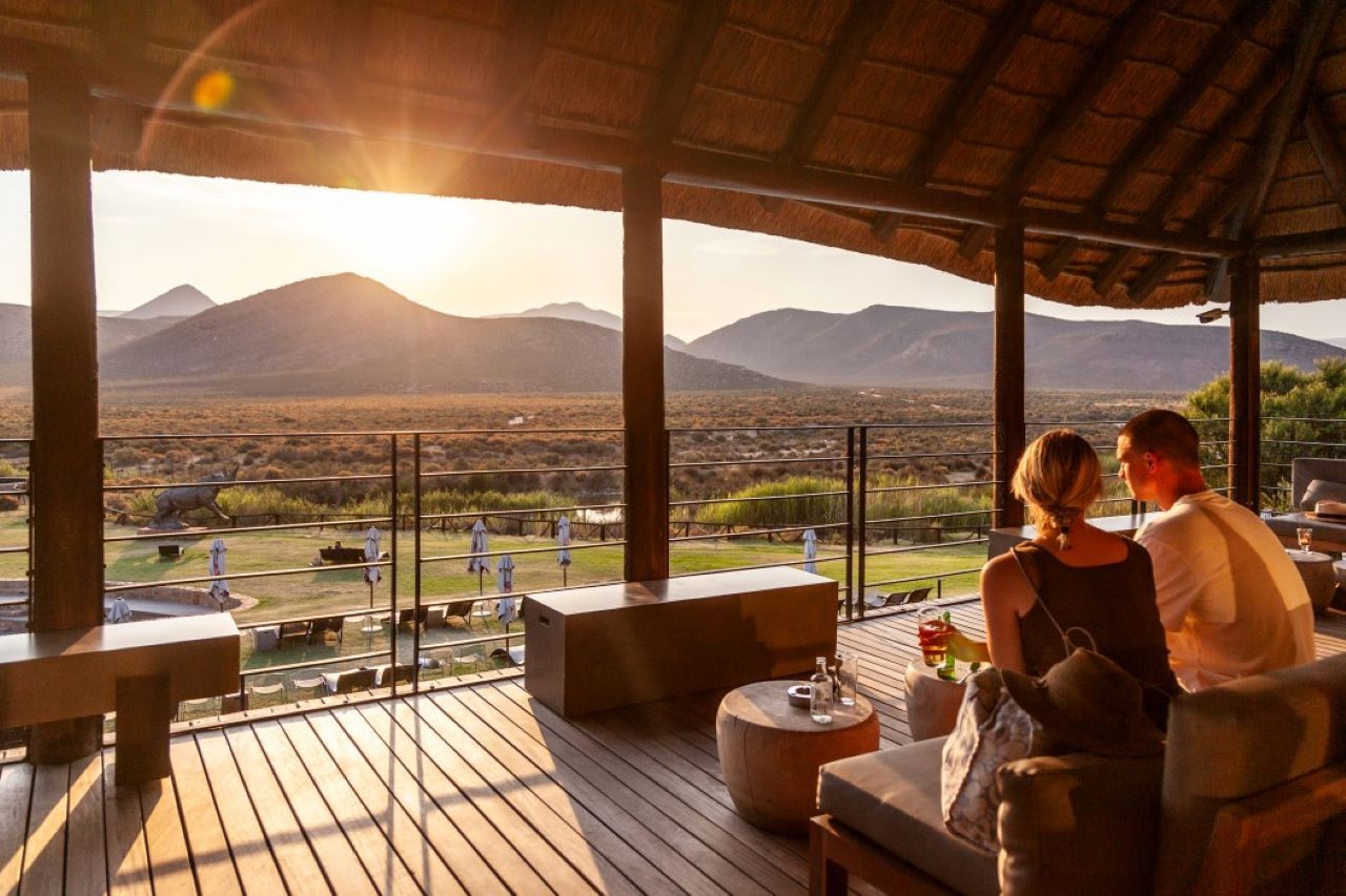 Couple seated on a patio, overlooking a landscape with mountains, and a setting sun.