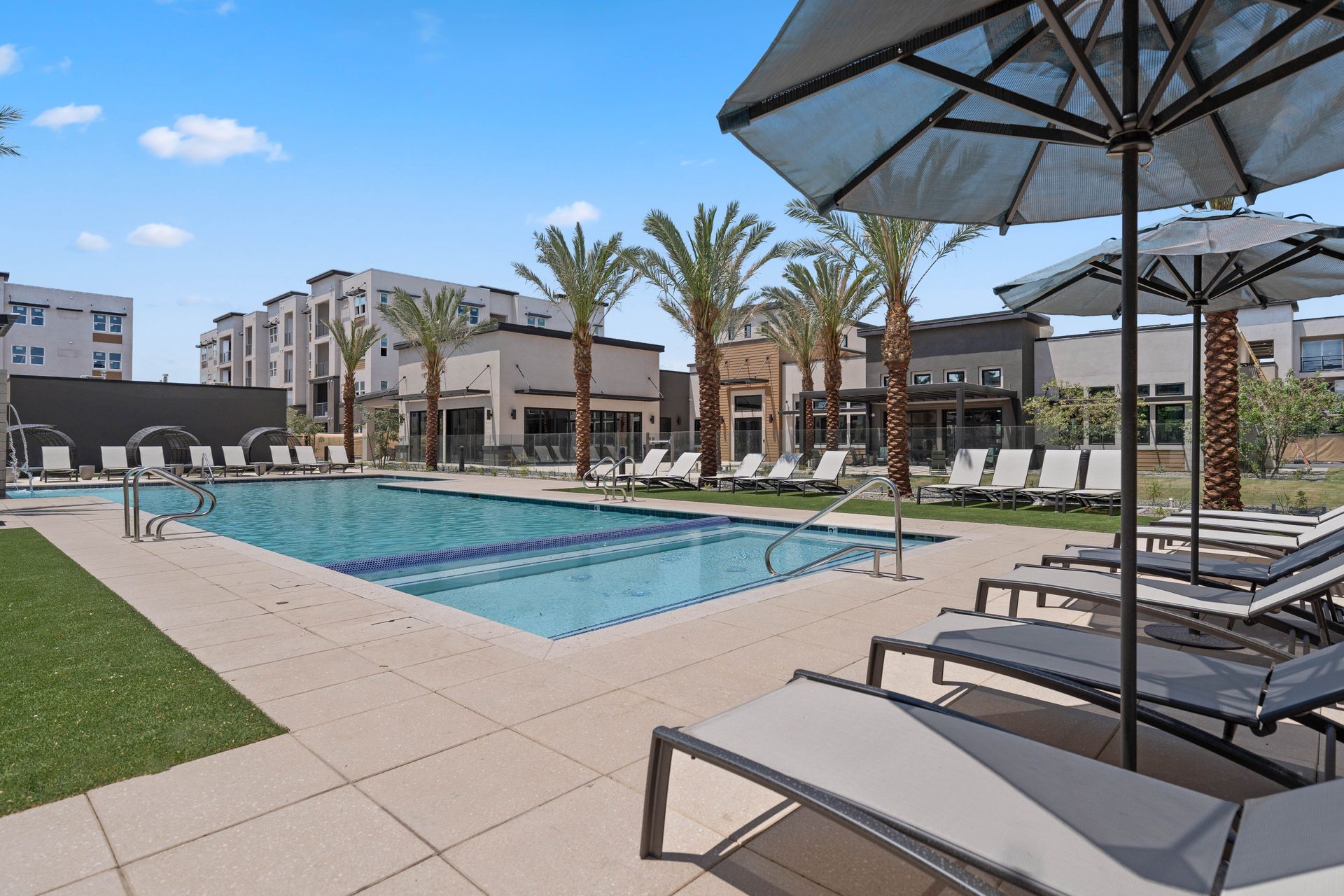 Swimming pool area with lounge chairs and umbrellas, buildings in the background.