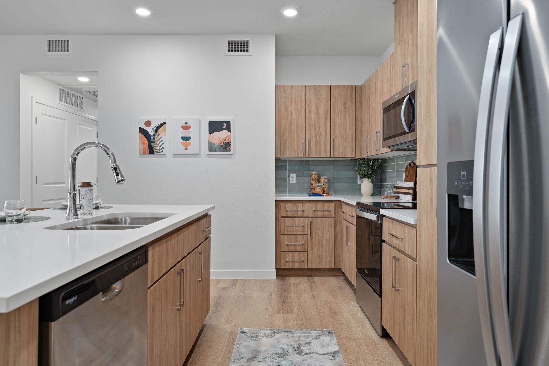 Modern kitchen with light wood cabinets, stainless steel appliances, and white countertops.