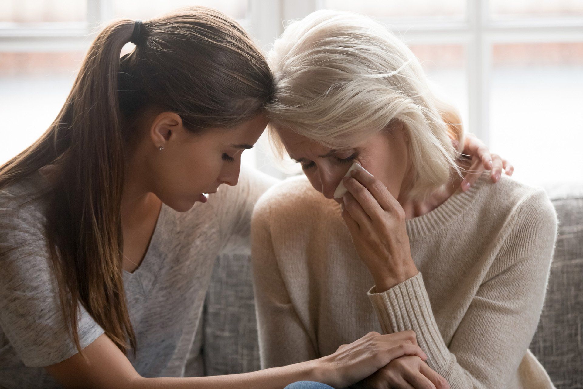 A young woman is comforting an older woman who is crying on a couch.