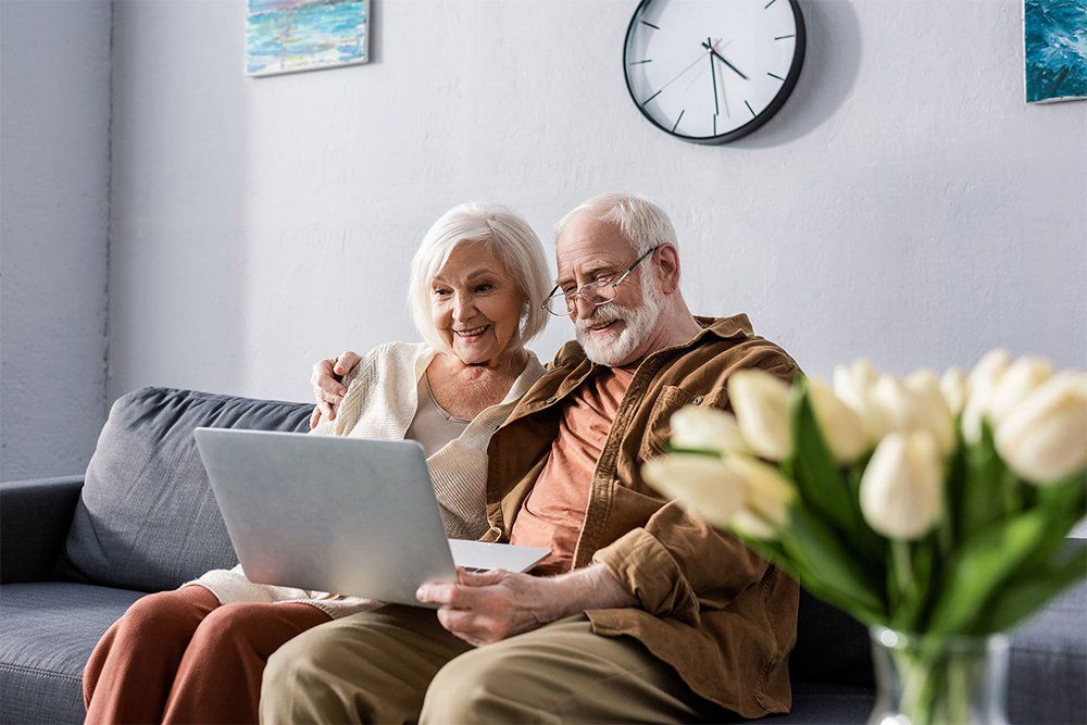 An elderly couple is sitting on a couch looking at a laptop.
