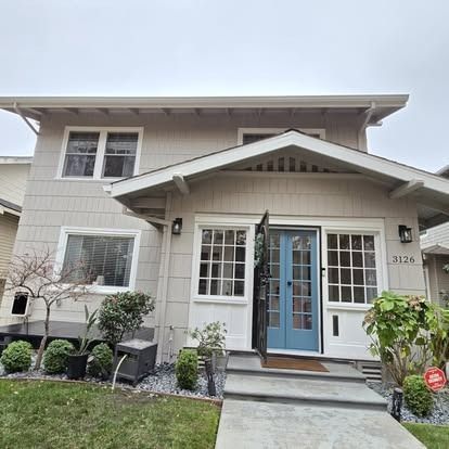 Light gray two-story house with blue front door, white trim, and small front yard with landscaping.