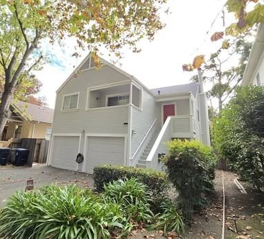 Two-story house with gray siding, two garage doors, stairs to the second floor, and landscaping.