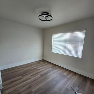 Empty room with wood-look floor, window with blinds, and ceiling light fixture.