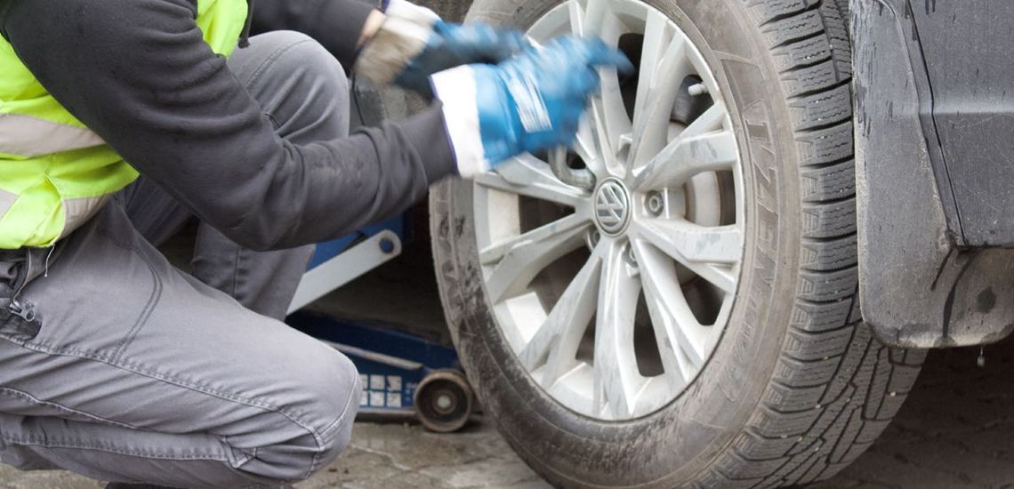 Person in gloves changing a car tire; vehicle jack visible.