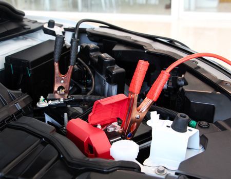 Car battery being jump-started with jumper cables. Red and black cables connected to terminals in engine bay.