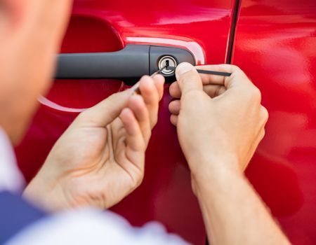 Person using lock picks to open a car door lock on a red car.